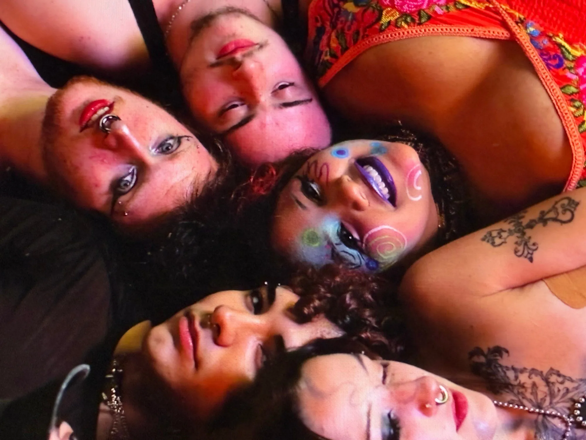 Overhead view of five people lying close together with colorful face paint and tattoos