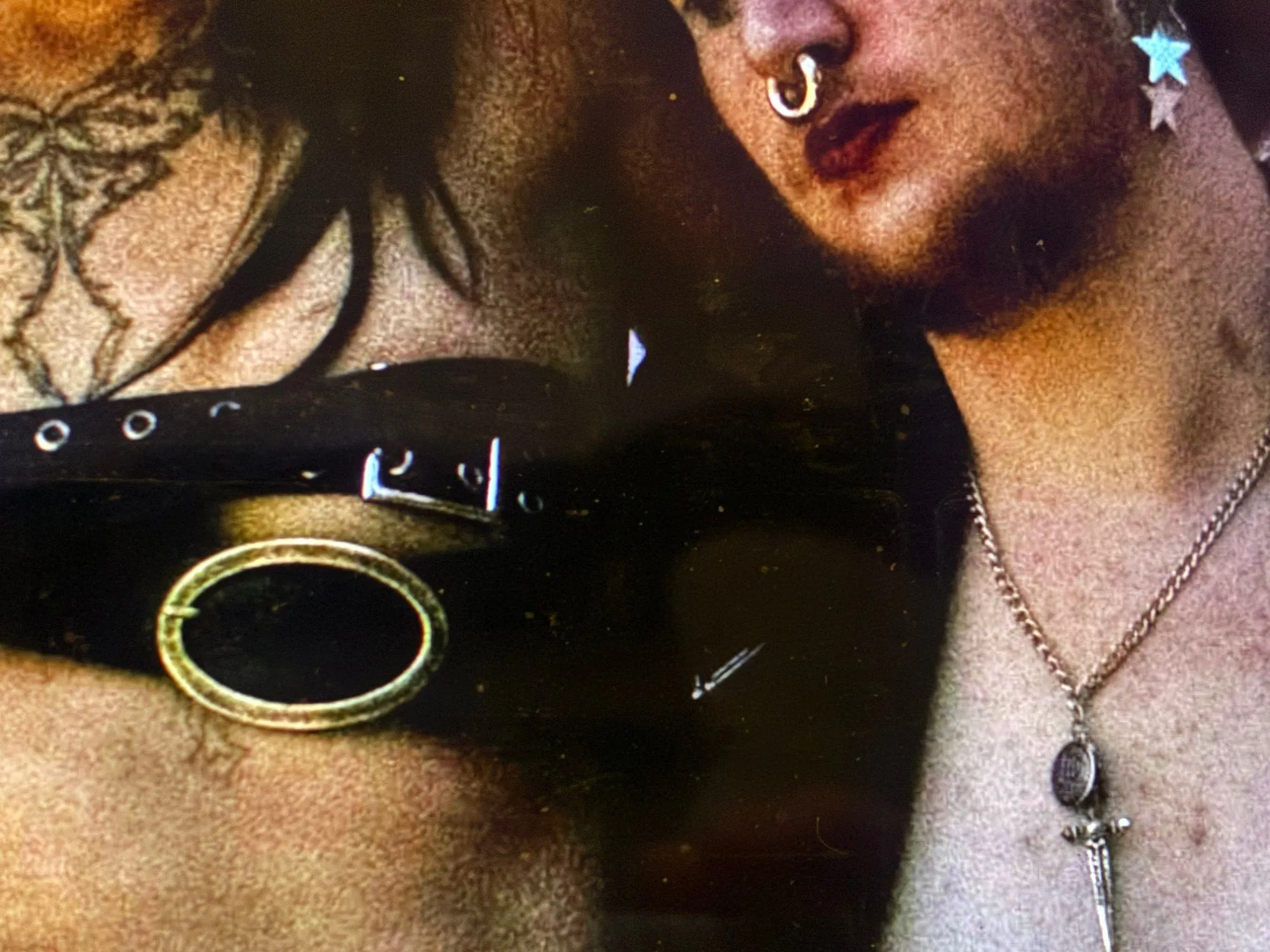 Close-up of a person with a nose ring, star earrings, and a dagger pendant necklace